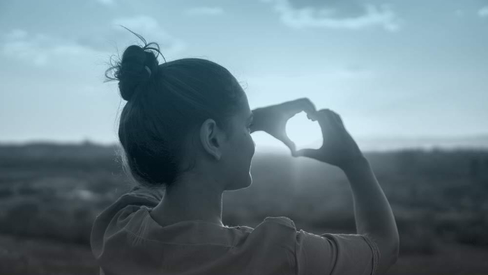 Girl looking through heart hands at sky