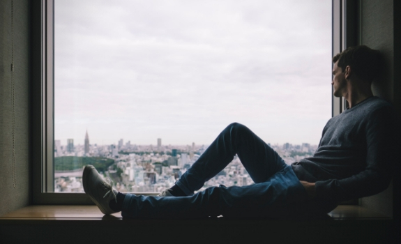 Man sitting on a window sill looking out at the city