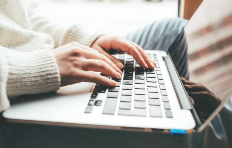 Person wearing a light coloured woolen jumper working on a Macbook Air