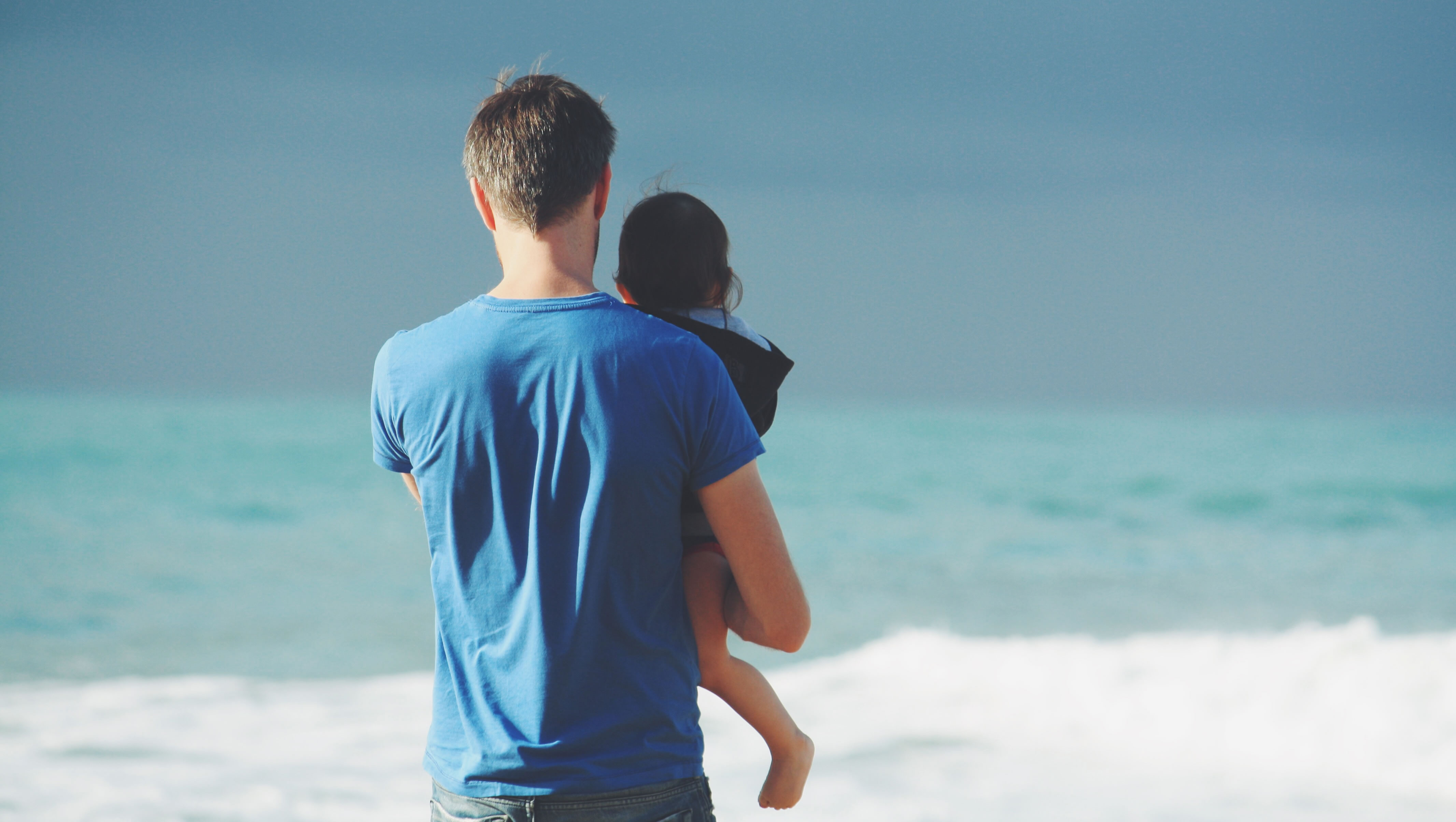 man holding child looking at waves